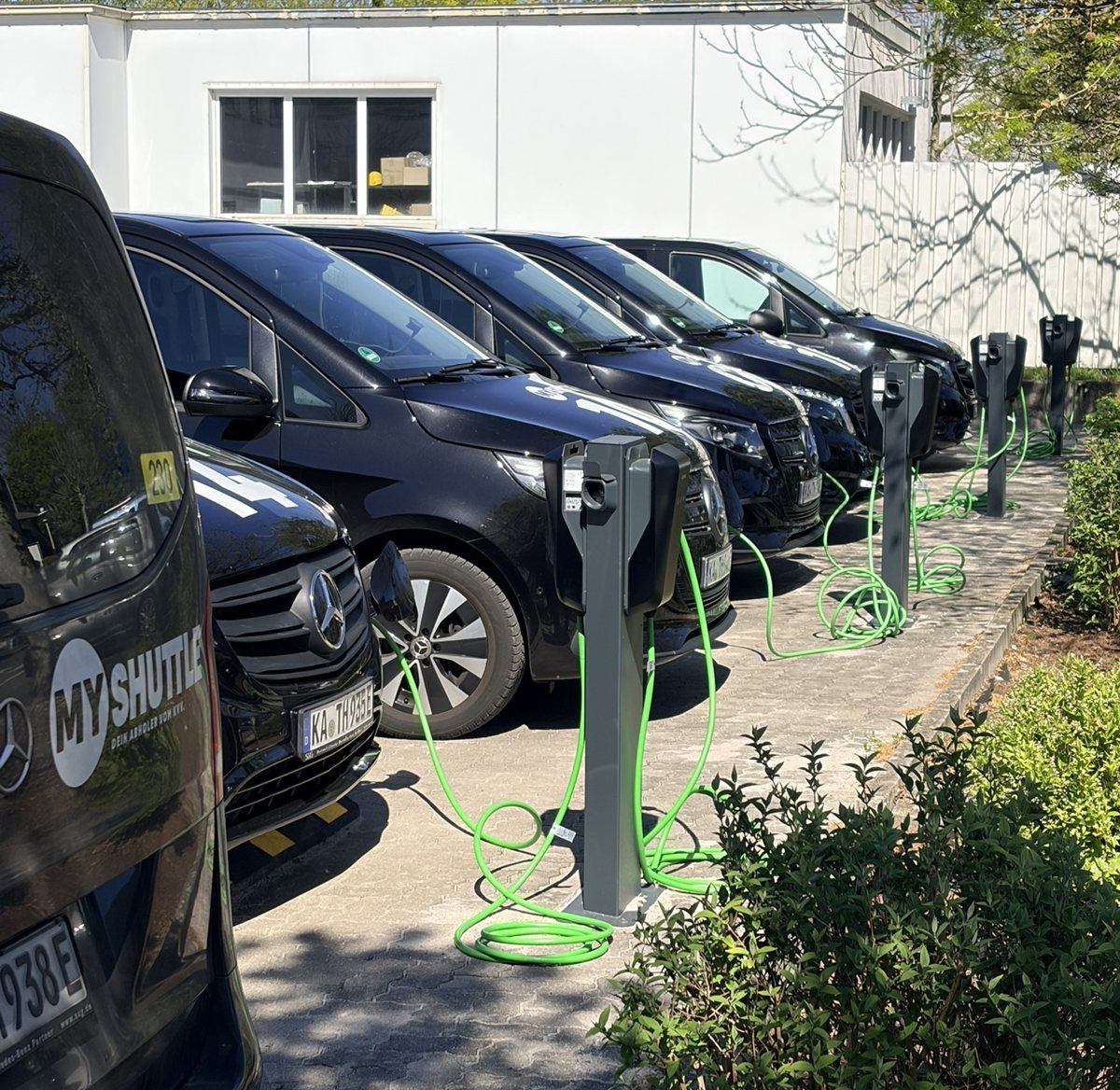 Reihe schwarzer Elektro-Vans der Holl AG an Ladesäulen mit grünen Ladekabeln