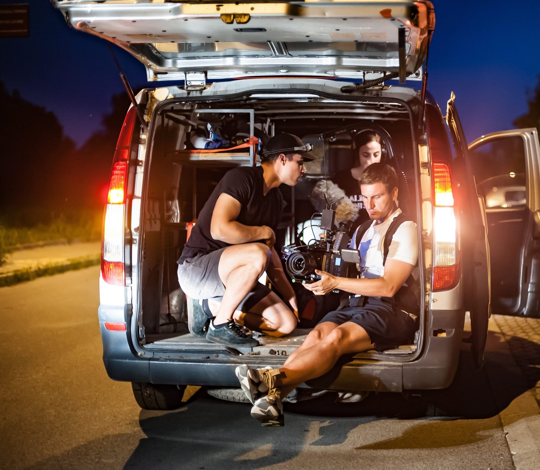 Filmcrew mit Kamera im geöffneten Heck eines Vans beim Nachtdreh